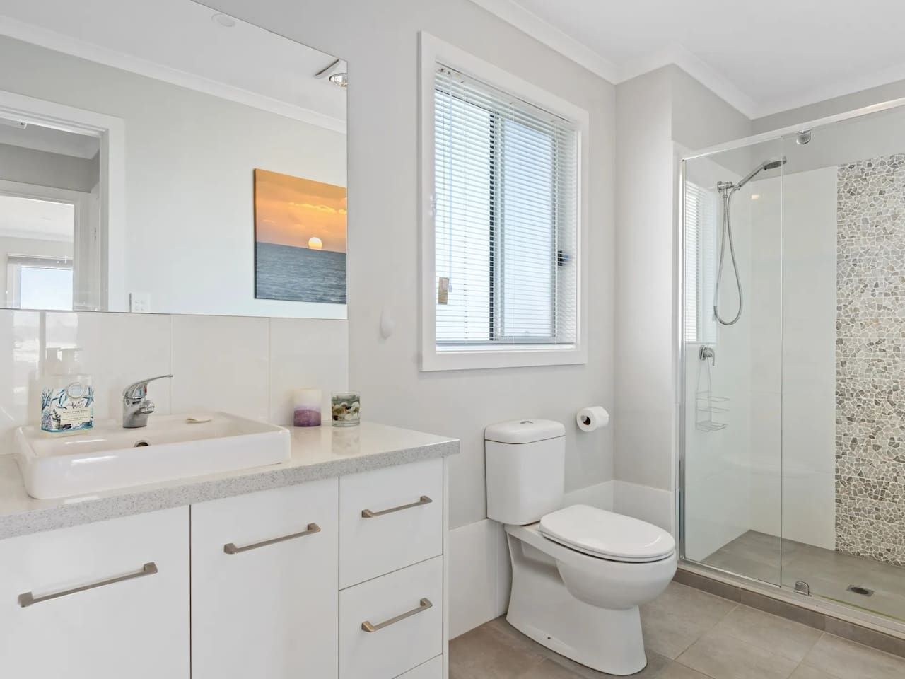 A modern bathroom with a glass shower enclosure, a toilet, and a sink with a mirror above.