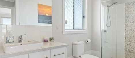 Un baño moderno con cabina de ducha de vidrio, inodoro y lavamanos con espejo.