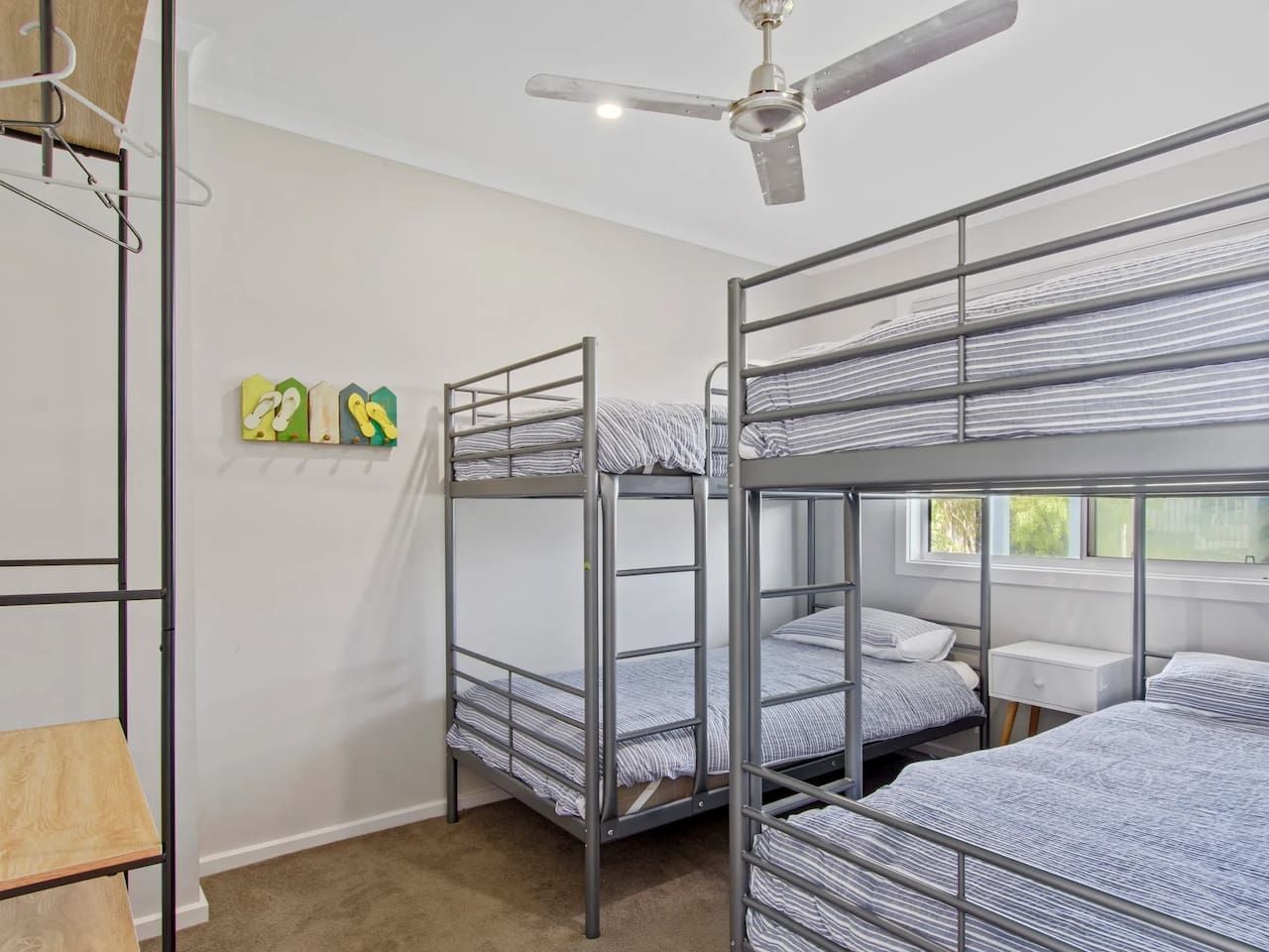 A dormitory room with bunk beds, a ceiling fan, a window, and a small bedside table.