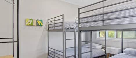 Un dormitorio con literas, ventilador de techo, ventana y una mesita de noche pequeña.