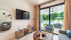 Un salon moderne doté d’un grand téléviseur, d’un meuble en bois, d’une table basse ronde agrémentée d’un objet décoratif, et offrant une vue sur une piscine et du mobilier d’extérieur.