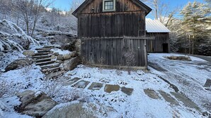 Eine rustikale Holzhütte mit einer Steintreppe, die zu ihr hinaufführt, umgeben von verschneitem Gelände und Bäumen.