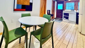 Ein Essbereich mit einem runden Tisch und vier grünen Stühlen, ein Holzboden, ein Küchenbereich mit Spüle und Schränken sowie ein großes abstraktes Gemälde an der Wand.