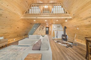 A log cabin interior with a loft bedroom, a sofa, a fireplace, and a staircase. - LAKESIDE DOCKSIDE: Henrys Fork Private Beach Dock Fishing Yellowstone UTV Snowmobile Trails (Island Park)