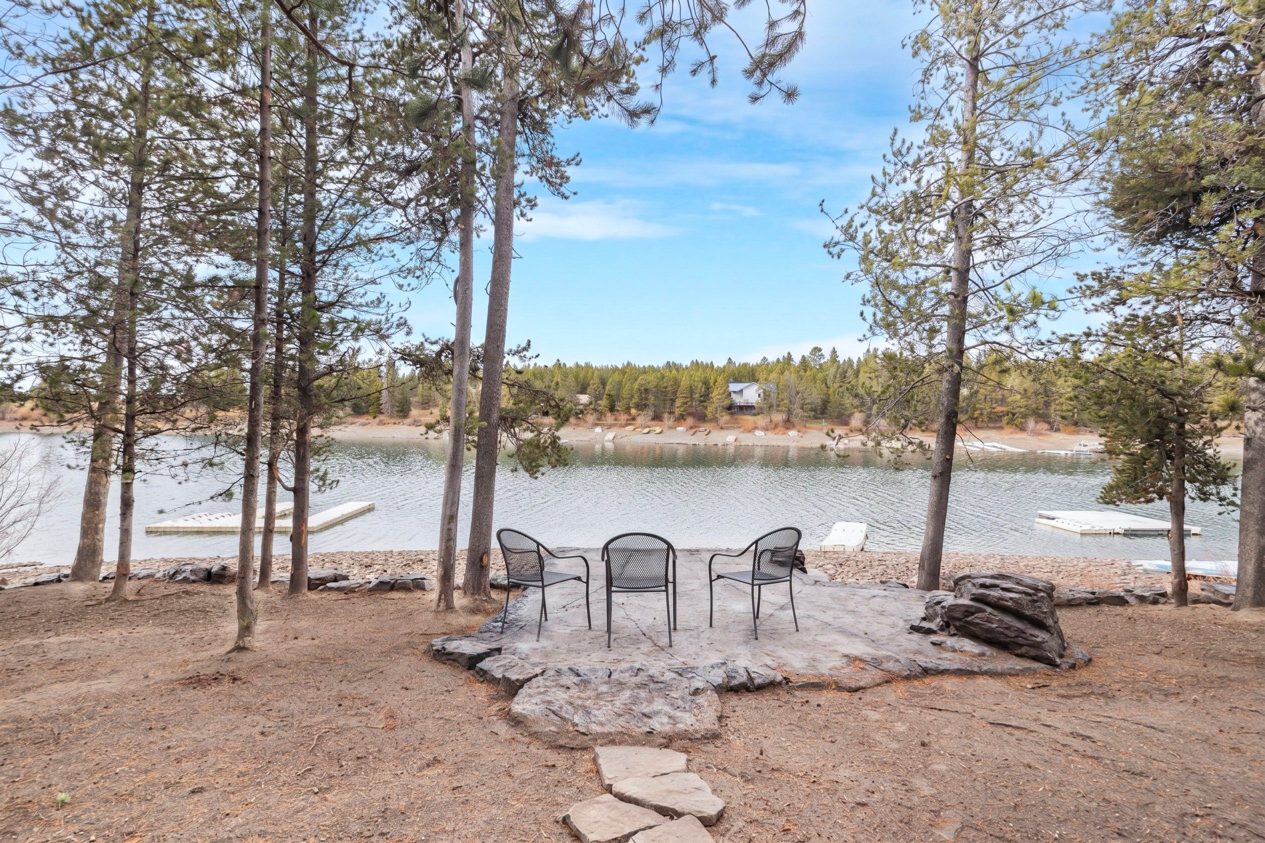 A lakeside seating area with a table and chairs, surrounded by trees and a view of the lake.