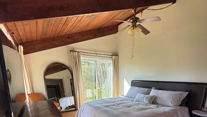 Ein Schlafzimmer mit Bett, Schreibtisch, Stuhl, Deckenventilator und einem großen Fenster.