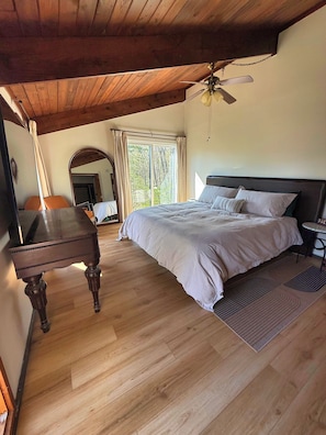 Un dormitorio con cama, escritorio, silla, ventilador de techo y una ventana grande.
