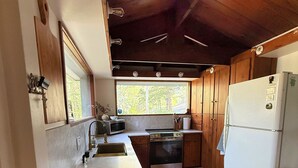 Eine Küche mit Holzschränken, einem weißen Kühlschrank, einer Spüle und einem Fenster mit Blick auf Bäume.
