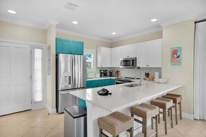 Une cuisine moderne avec des meubles blancs, des touches de couleur turquoise, des appareils en acier inoxydable et un îlot central doté de tabourets de bar.