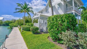 A white coastal house with a covered porch, a grassy lawn, and a palm tree. - The Point at Coral Lagoon, Rare End of Canal Villa (Marathon)