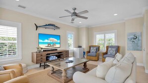 A living room with a television, a ceiling fan, wicker furniture, and a large window with blinds. - The Point at Coral Lagoon, Rare End of Canal Villa (Marathon)