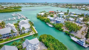 A marina with several boats docked, surrounded by residential buildings with modern architecture, and a clear view of the coastline. - The Point at Coral Lagoon, Rare End of Canal Villa (Marathon)