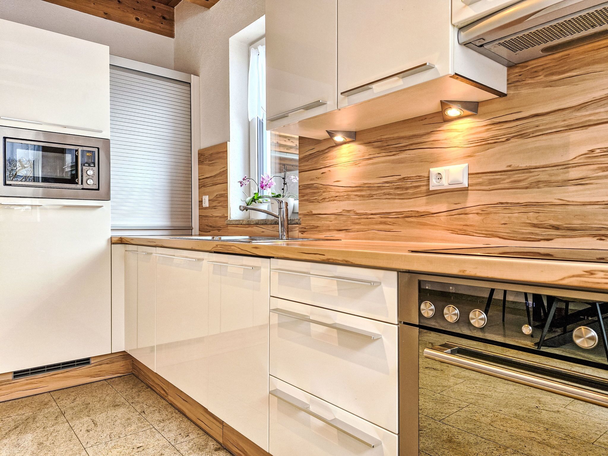 A modern kitchen with white cabinetry, a wooden backsplash, a built-in oven, and a microwave.