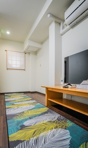 A room with a large window, an air conditioning unit, a wooden desk, and a colorful patterned rug. - meisei nihonya (Osaka)