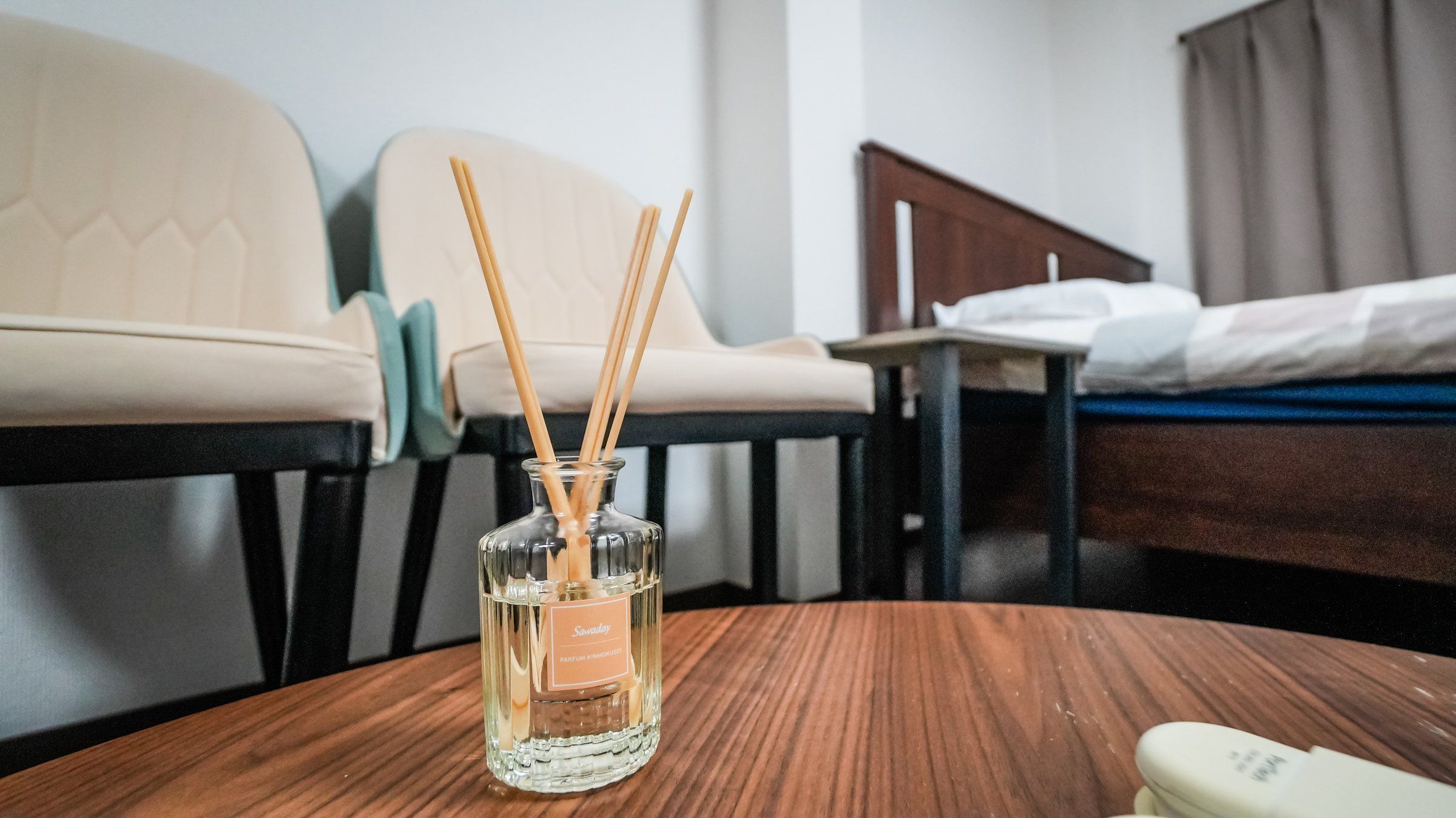 A hotel room with a wooden table, a bottle of perfume, and a bed with a white comforter.