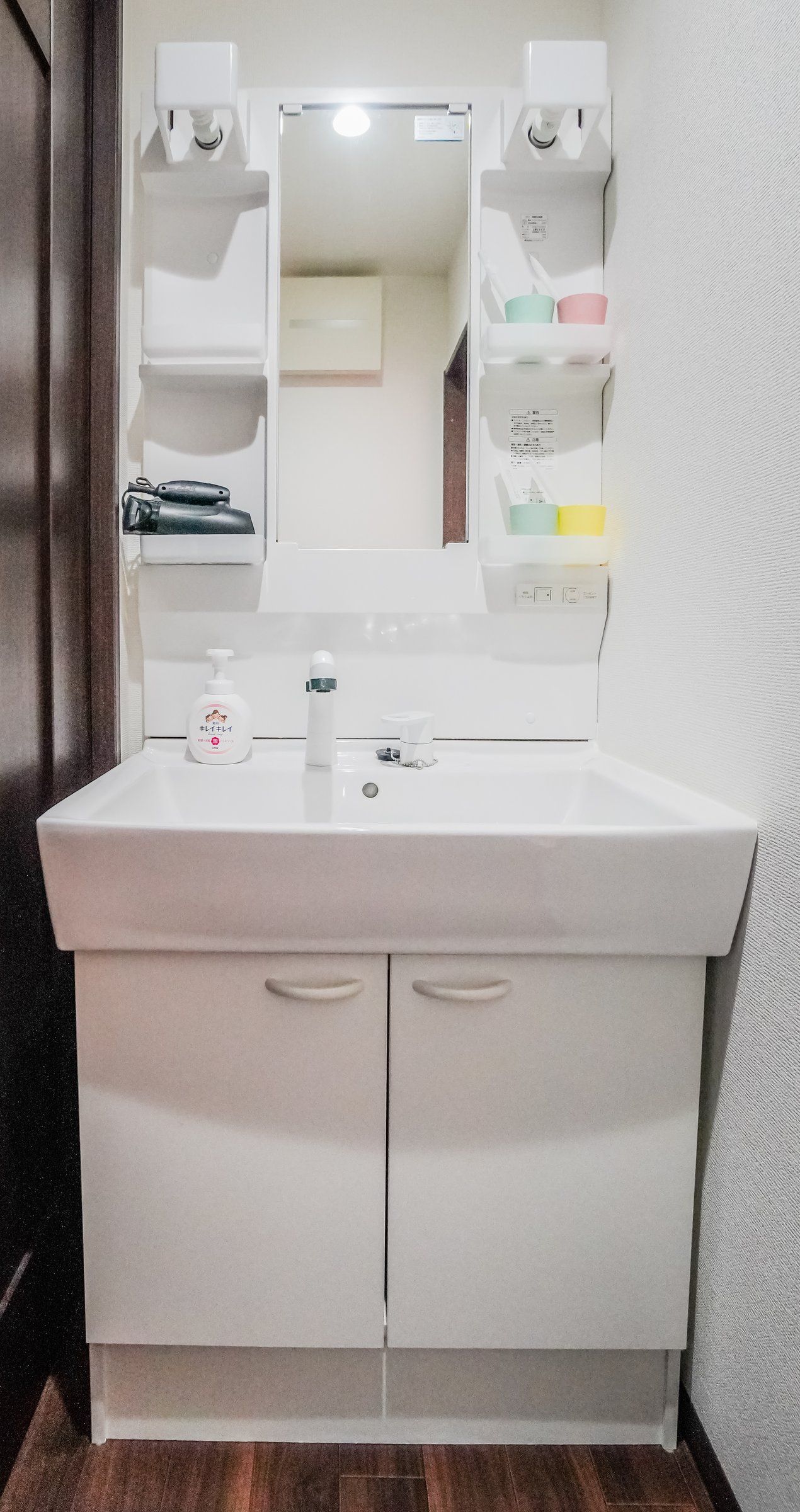 A bathroom with a white sink, a mirror, and a shelf with toiletries.