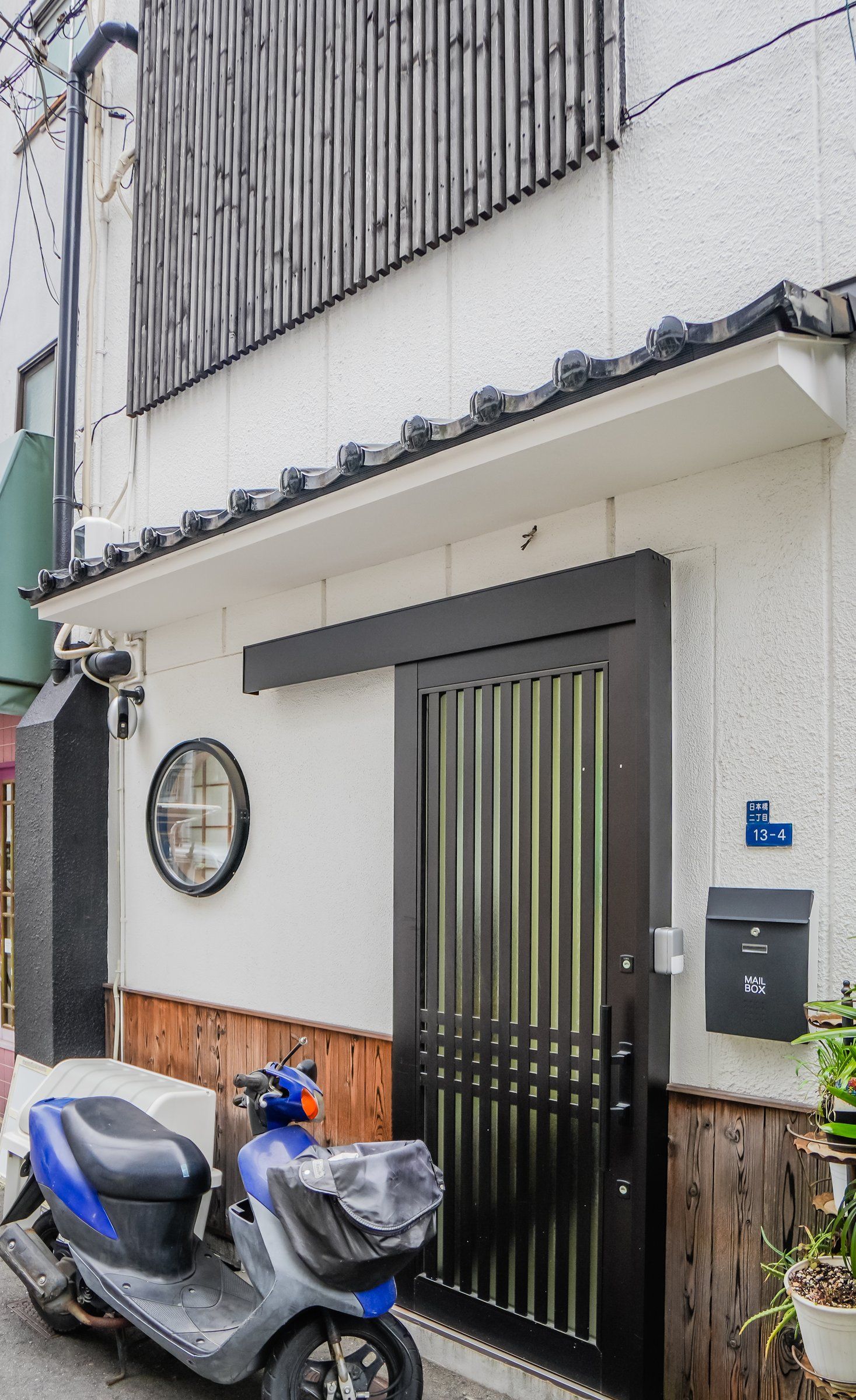 A residential building with a black gate, a mail box, and a blue scooter parked in front.