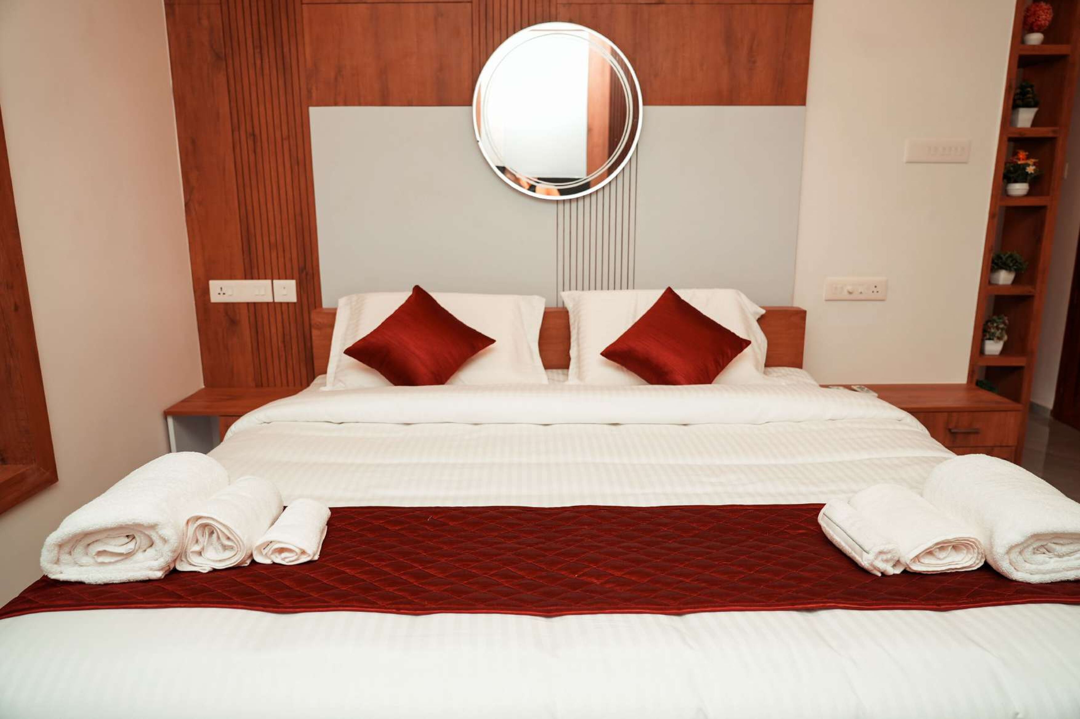 Habitación de hotel con una cama grande, dos almohadas, una colcha acolchada roja y un espejo redondo sobre la cama.