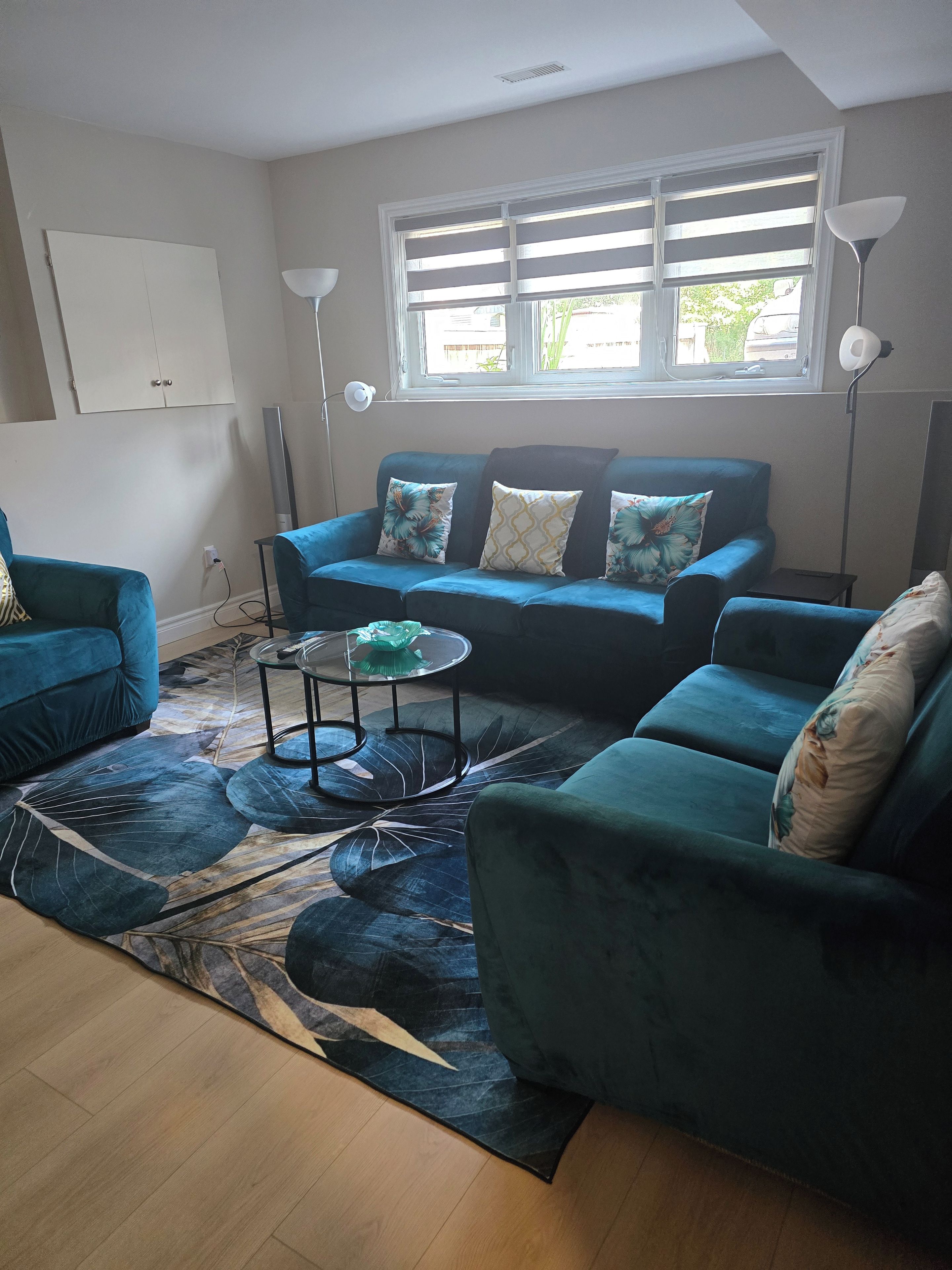 A living room with a blue sofa set, a glass coffee table, and a patterned rug.