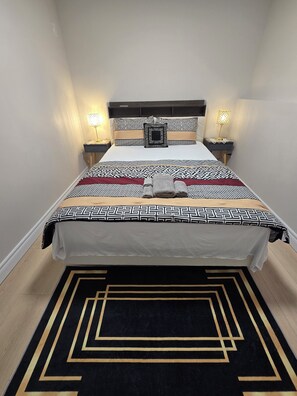 A neatly made bed with a patterned bedspread, two bedside lamps, and a decorative pillow. - Clean Comfy 2 Bedroom Suite near Niagara Falls (St. Catharines)