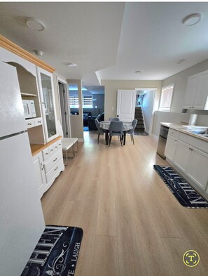 A modern kitchen with white cabinets, a dining area with a table and chairs, and a visible staircase leading to another level. - Clean Comfy 2 Bedroom Suite near Niagara Falls (St. Catharines)