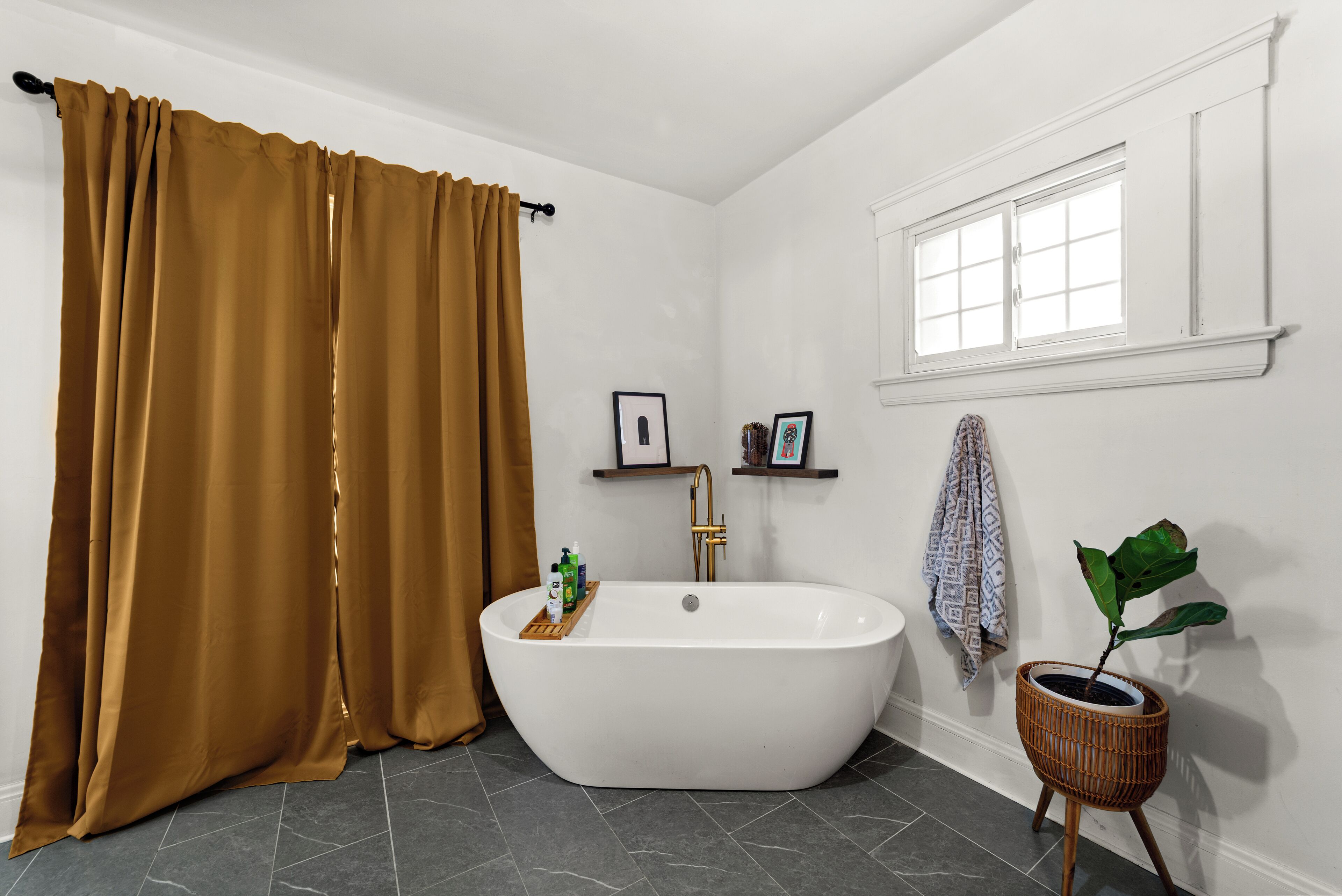 Een badkamer met een vrijstaand bad, een raam, een potplant en een handdoek aan de muur.