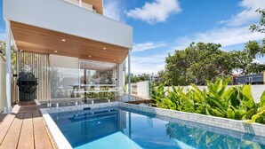 Ett modernt hus med en swimmingpool, ett trädäck och frodig grönska.