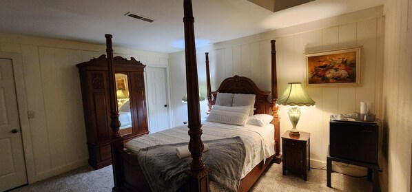 A four-poster bed with a mirror and a nightstand with a lamp.
