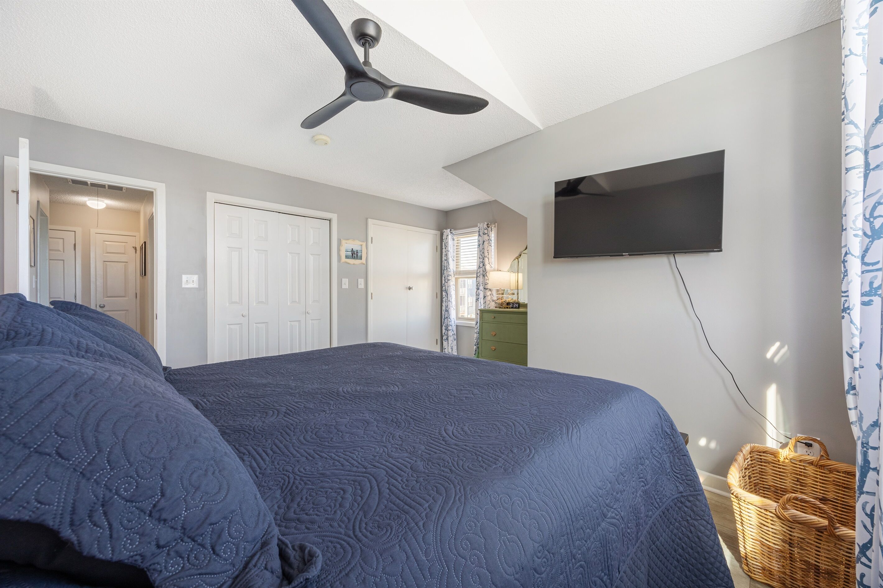 A bedroom with a large bed, a ceiling fan, a flat-screen TV, and a wicker basket.