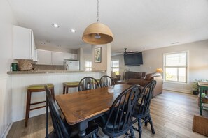 Un'area pranzo con un tavolo e sedie in legno, una lampada a sospensione e una cucina sullo sfondo.