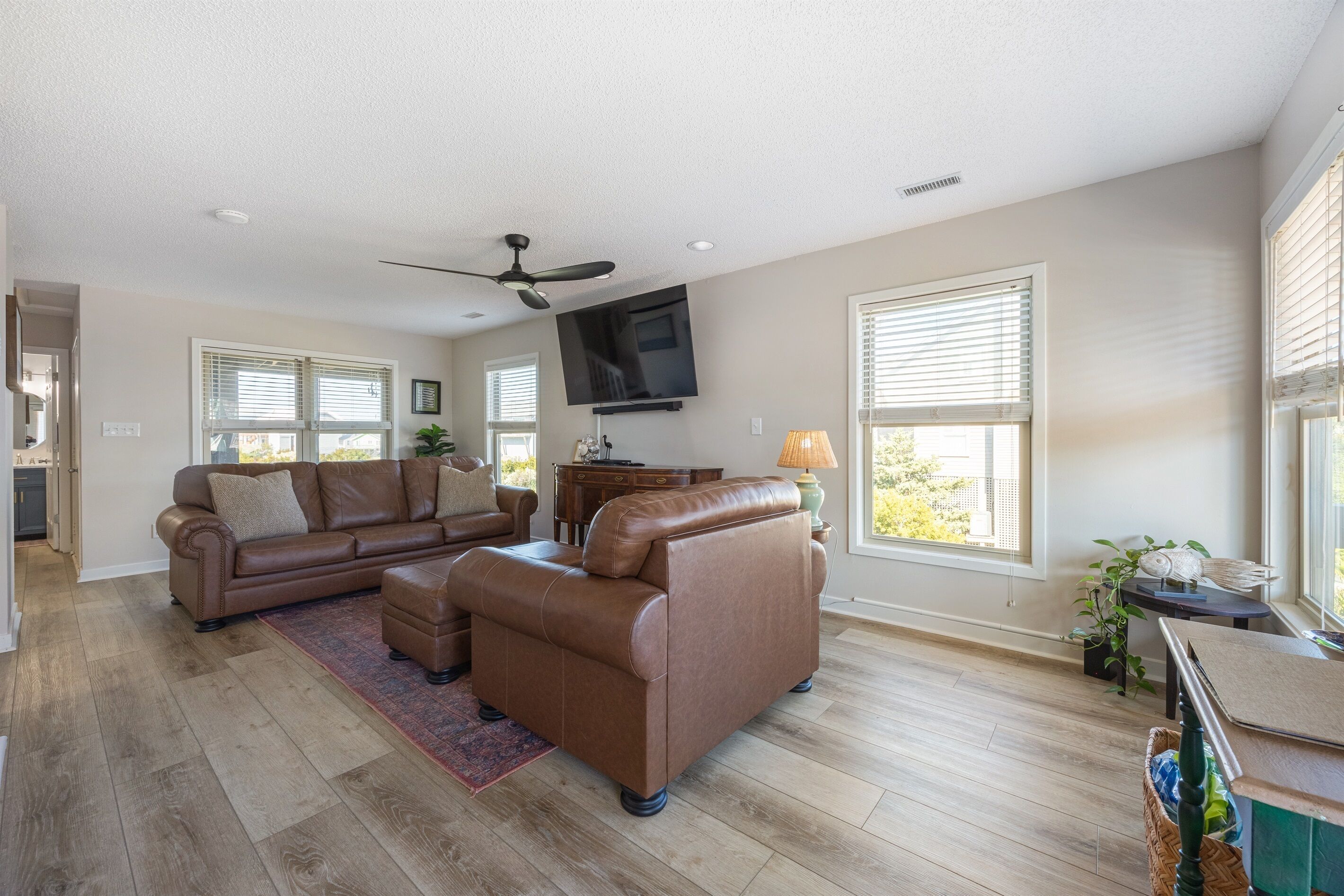 A spacious living room with a brown leather sofa, a coffee table, and a television mounted on the wall.