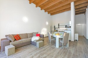Ein modernes Wohnzimmer mit einer Couch, einem Hocker und einem Esstisch mit Stühlen.