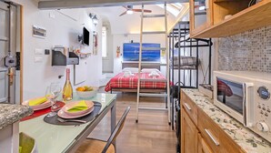 Habitación compacta con literas, kitchenette, comedor con mesa para dos y televisión montada en la pared.