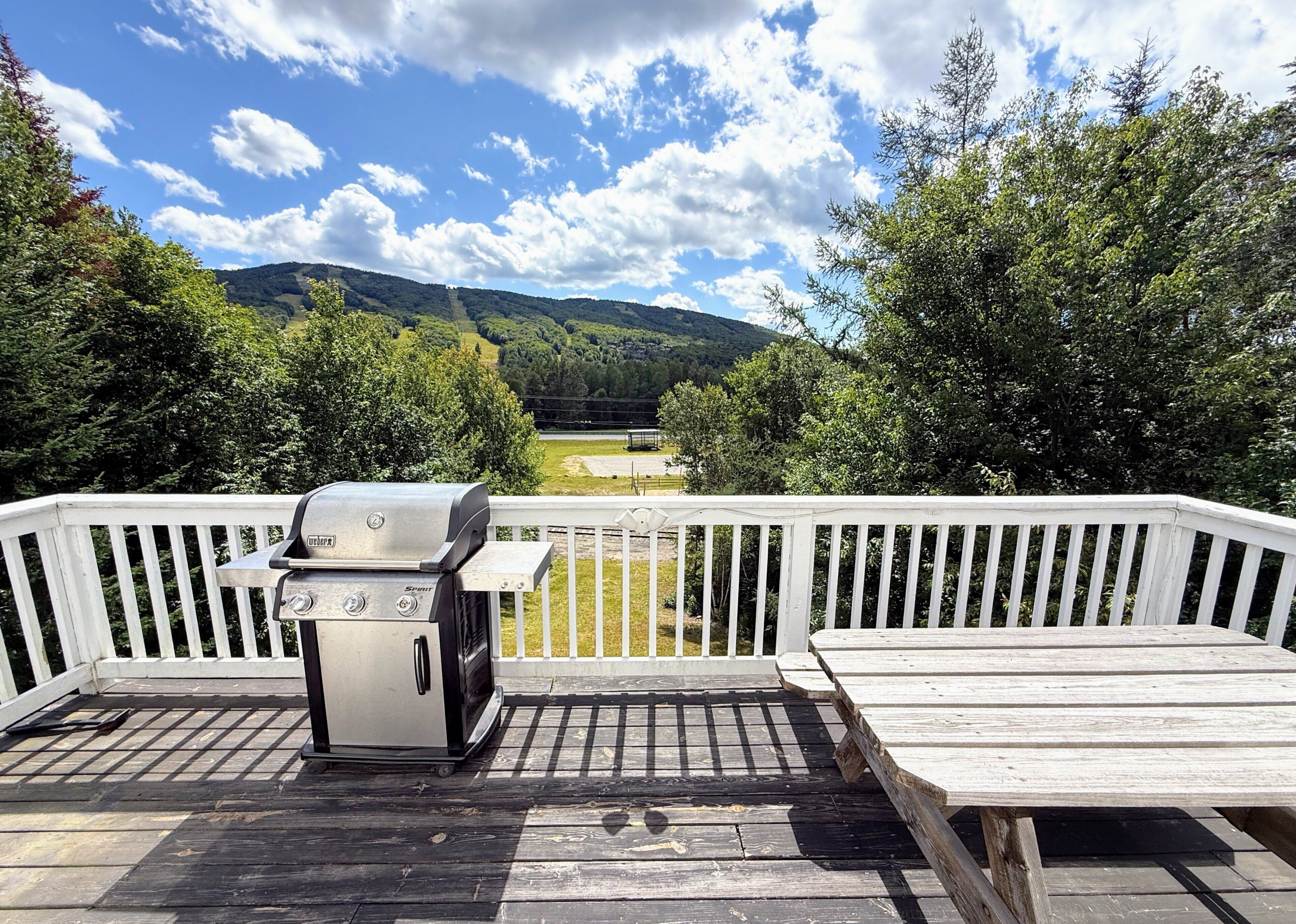 A deck with a barbecue grill, a bench, and a view of a forested area with hills.