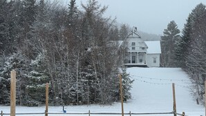 Un espace extérieur enneigé, avec une clôture en bois, des chaises Adirondack rouges et un bâtiment blanc en arrière-plan.