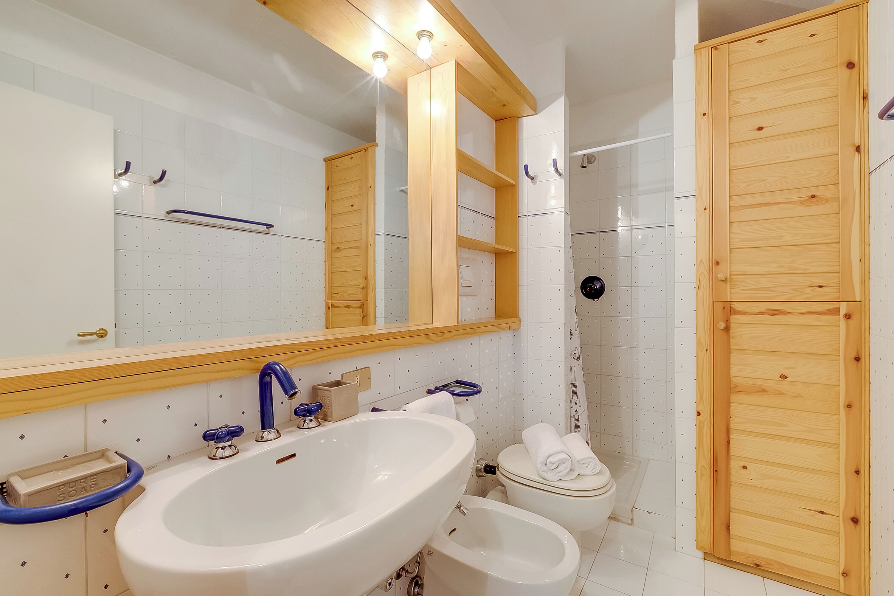 A modern bathroom with a large white sink, a mirror, and a wooden shower enclosure.