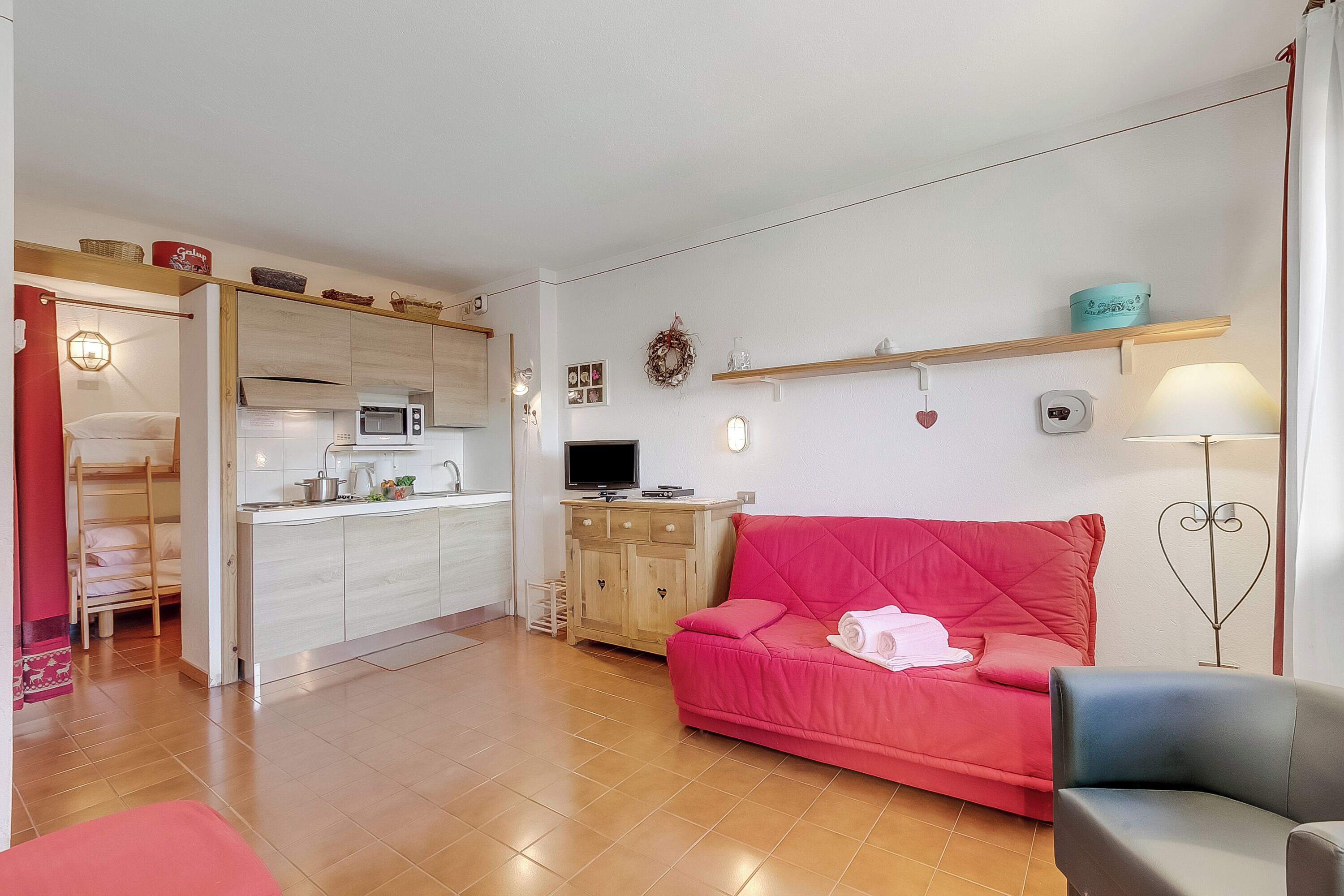 A compact living space with a kitchenette, a red sofa, a blue armchair, and a small dining table.