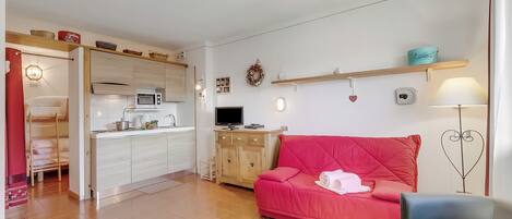 A compact living space with a kitchenette, a red sofa, a blue armchair, and a small dining table.