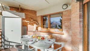 A dining area with a table set for two, a brick wall, a window with a view, and an air conditioning unit.