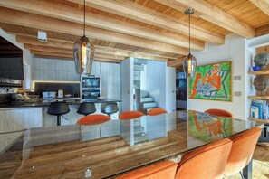 Una cocina moderna con vigas de madera, una mesa de comedor de cristal y sillas naranjas.