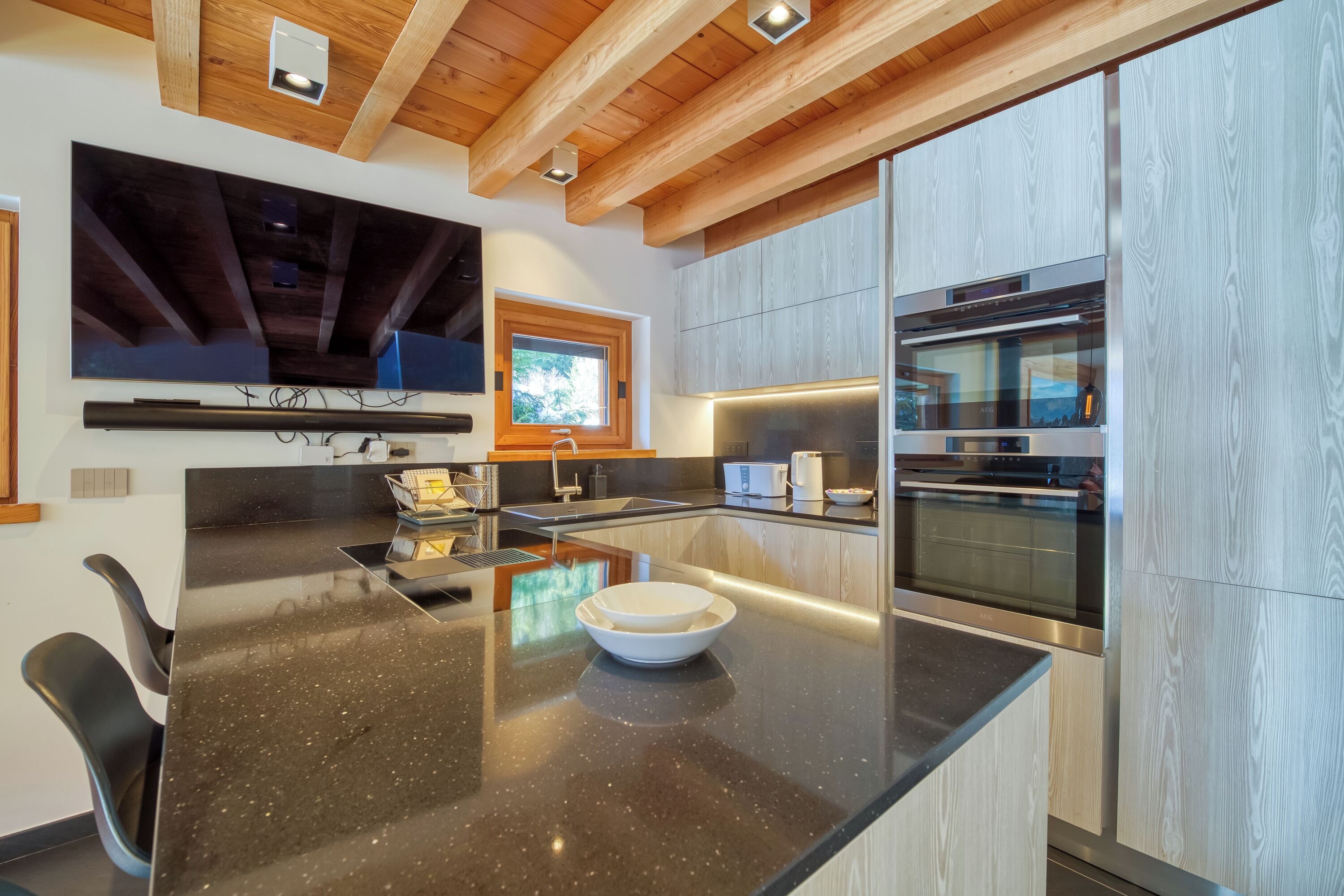 A modern kitchen with a large island, built-in appliances, and a wooden ceiling.
