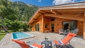 Una cabaña de madera con piscina, mobiliario exterior y vistas a las montañas.