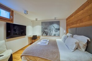 Un dormitorio con cama, escritorio, silla, televisor y un cuadro.