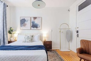 A modern bedroom with a large bed, bedside tables, a floor lamp, and abstract wall art. - Chic Studio Apartment on Oglethorpe Square (Savannah)