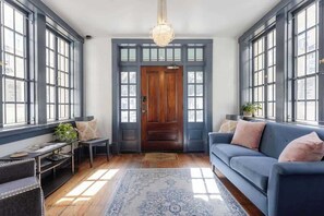 A spacious room with large windows, a wooden door, a blue sofa, and a chandelier. - Chic Studio Apartment on Oglethorpe Square (Savannah)