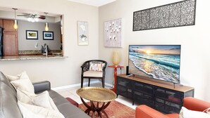 Een woonkamer met een grijze bank, een rode fauteuil, een salontafel en een televisie op een zwarte standaard.