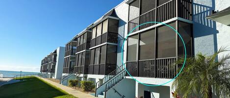 A modern multi-story building with balconies and large windows, located near a body of water.
