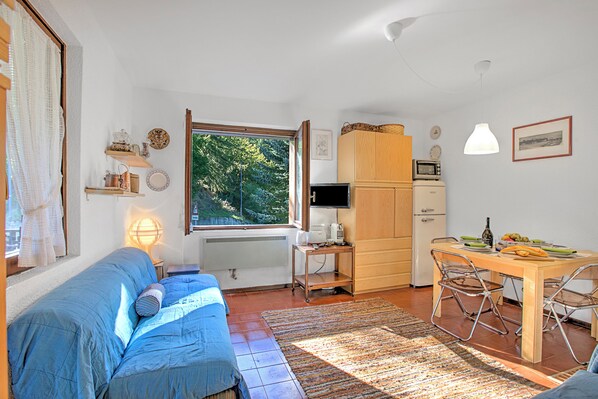 A compact living space with a bed, a desk, a dining table, and a view of greenery through a window. - Appartamento Chez Mavi Cond Il Rio for 4, Sauze d'Oulx, Italy (Sauze d'Oulx)
