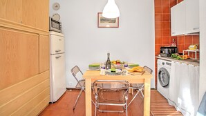 A compact kitchen with a wooden cabinet, a white refrigerator, a hanging pendant light, and a dining table with chairs. - Appartamento Chez Mavi Cond Il Rio for 4, Sauze d'Oulx, Italy (Sauze d'Oulx)