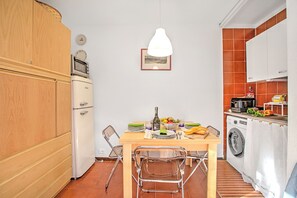 A compact kitchen with a wooden cabinet, a white refrigerator, a hanging pendant light, and a dining table with chairs. - Appartamento Chez Mavi Cond Il Rio for 4, Sauze d'Oulx, Italy (Sauze d'Oulx)